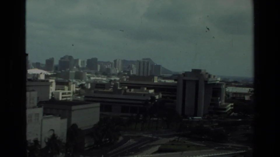 1981 Hawaii 8mm frame showing an elevated city view with high-rises, low rooftops, cloudy sky, and Diamond Head in the distance.