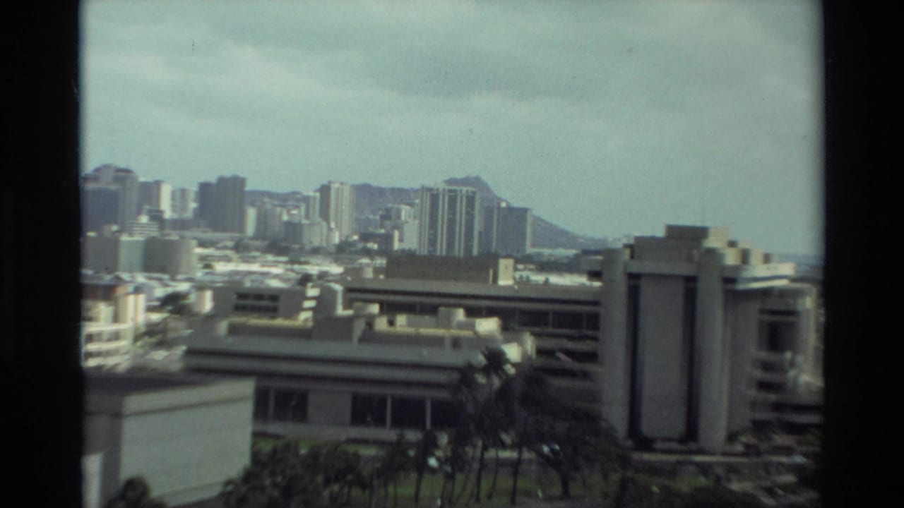 Visitor-shot 1981 Hawaii view across urban buildings toward Diamond Head, with soft focus and visible 8mm frame borders.