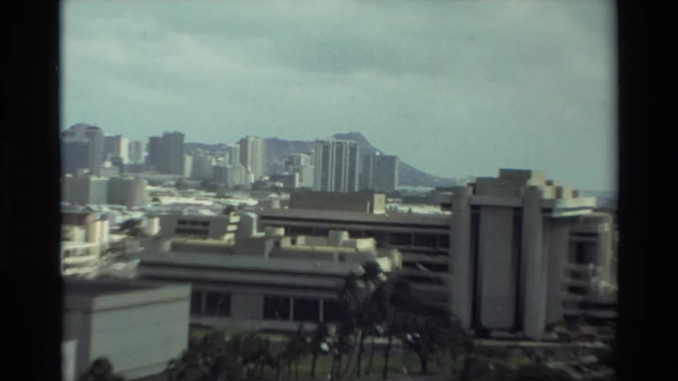 Visitor-shot 1981 Hawaii view across urban buildings toward Diamond Head, with soft focus and visible 8mm frame borders.