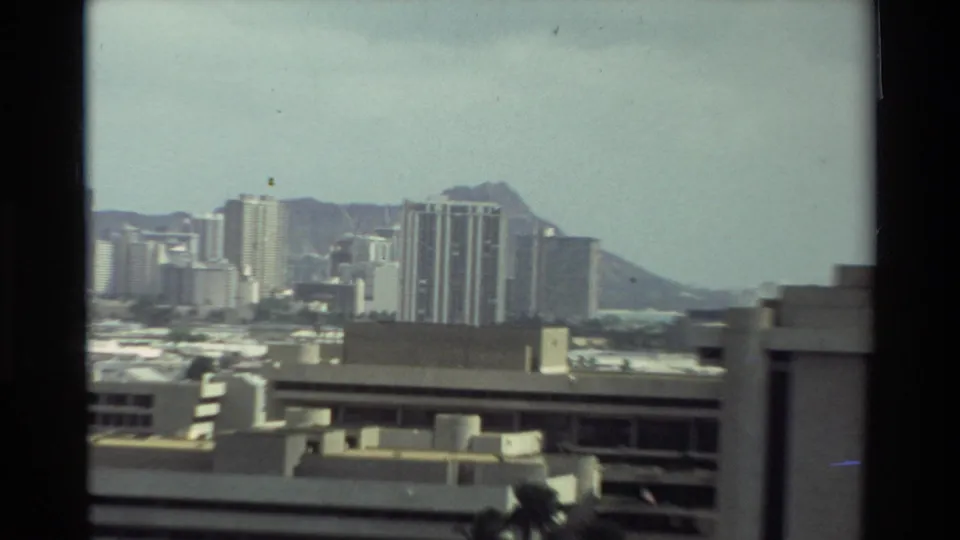 1981 Hawaii 8mm frame with tall urban towers, a low foreground building, distant ocean, and Diamond Head under a pale sky.