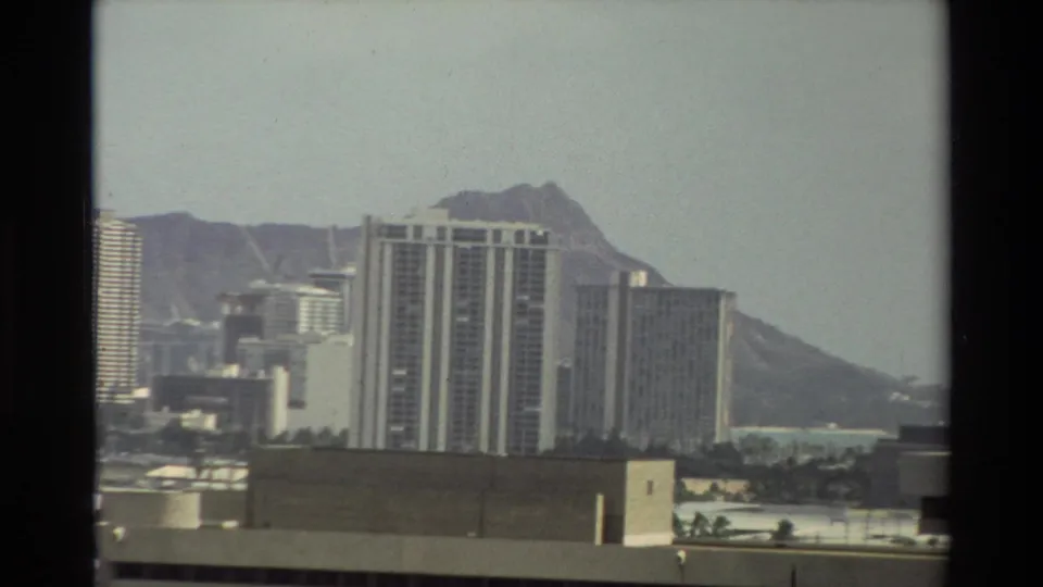 1981 Hawaii 8mm frame centering tall city buildings with Diamond Head behind them and low rooftops in the foreground.