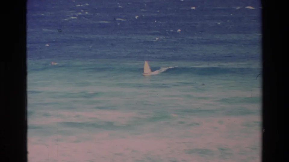 Distant windsurfer on blue and turquoise Hawaii surf, with soft grain and faded 8mm color.