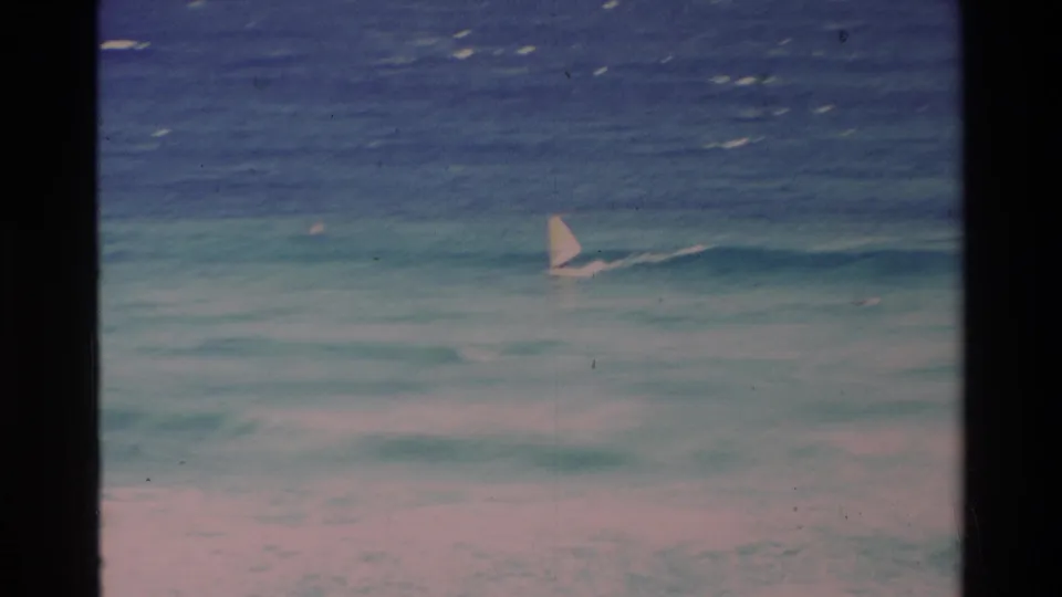 1981 Hawaii 8mm frame of a lone windsurfer cutting across layered turquoise surf.
