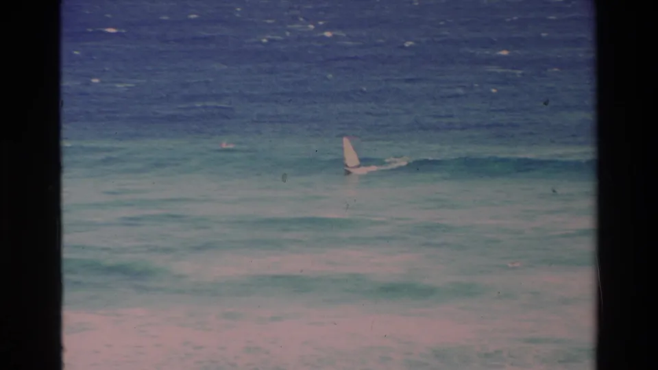 1981 Hawaii 8mm frame showing a small white sail moving across blue-green ocean waves, with dark film borders and visible grain.