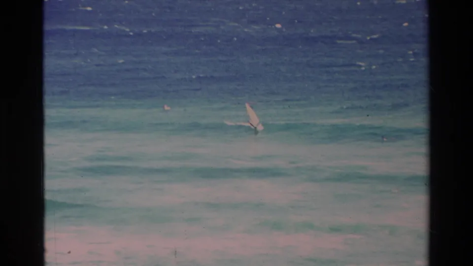 8mm home-movie frame from Hawaii in 1981 showing a distant small sail against pale foam and blue-green surf.