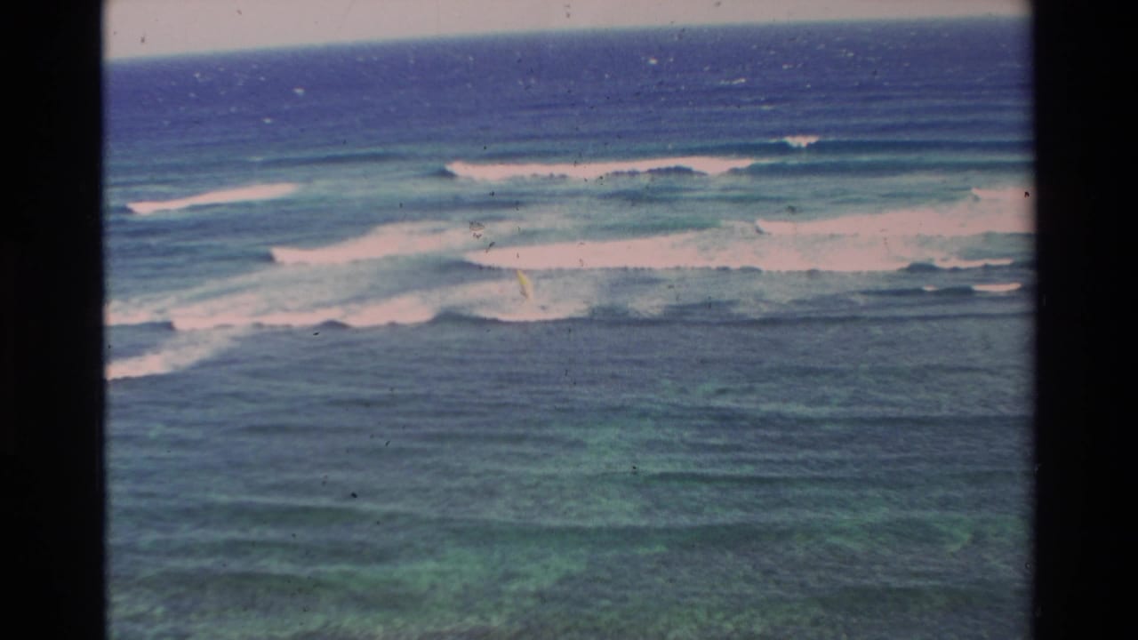 1981 Hawaii frame with a distant windsurfer on blue-green water beyond lines of breaking surf.