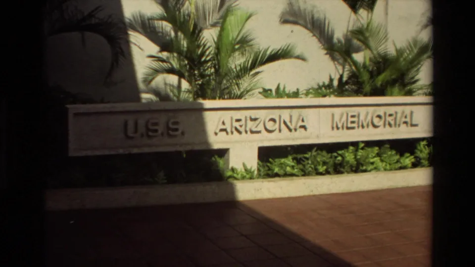 1981 Hawaii visitor-area frame showing U.S.S. Arizona Memorial signage, tropical plantings, palm fronds, and pavement.