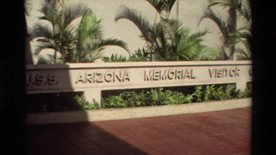 1981 Hawaii frame showing U.S.S. Arizona Memorial visitor signage with palms, low planting beds, and reddish pavement.