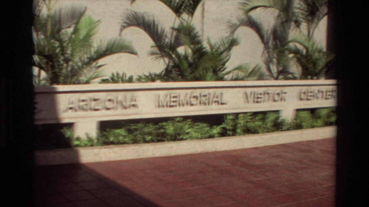 Engraved Arizona Memorial Visitor Center sign with palm landscaping and red paving.