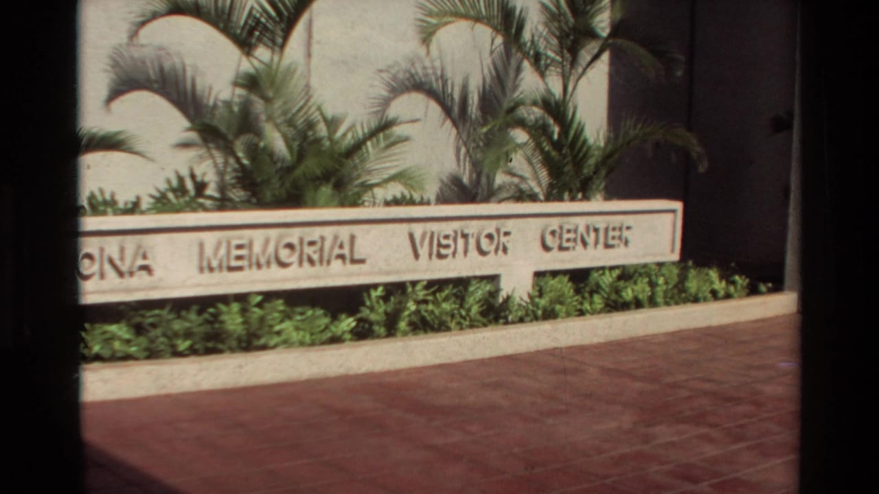 1981 Hawaii frame with the visitor center sign, palm plantings, red paving, and a dark vertical obstruction across the view.