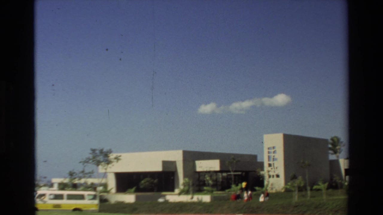 1981 Hawaii home-movie view of the USS Arizona Memorial exterior with visitors, landscaping, blue sky, and a van in the foreground.