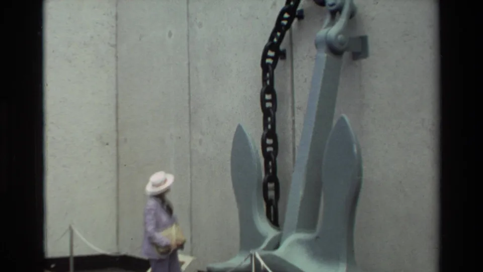 Visitor passes the USS Arizona anchor at Pearl Harbor, with the concrete memorial wall and roped barrier visible.
