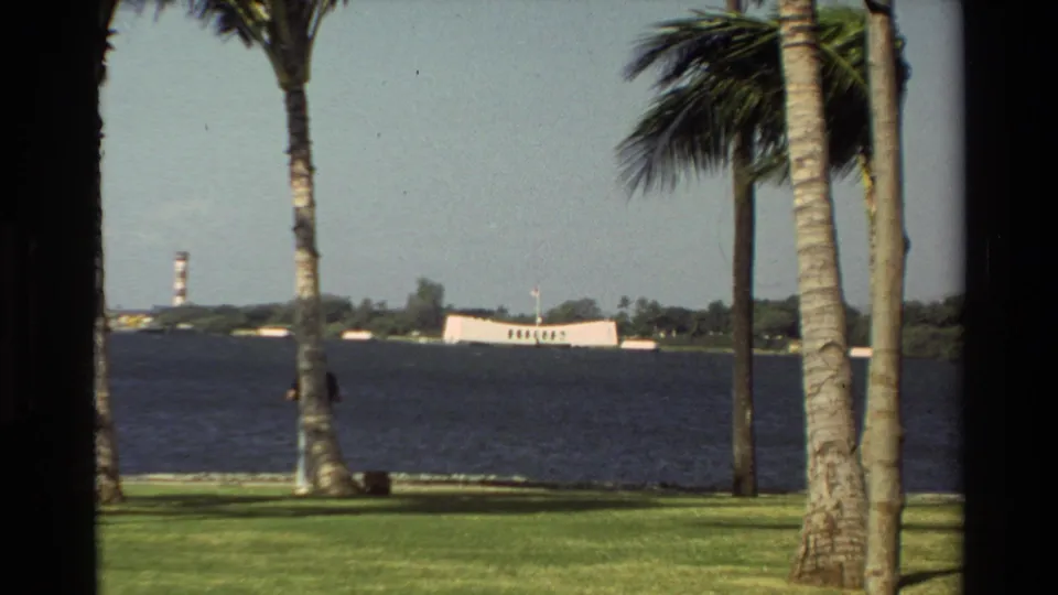 1981 Hawaii home-movie frame showing palm trees, open water, shoreline, and the USS Arizona Memorial visible in the distance.