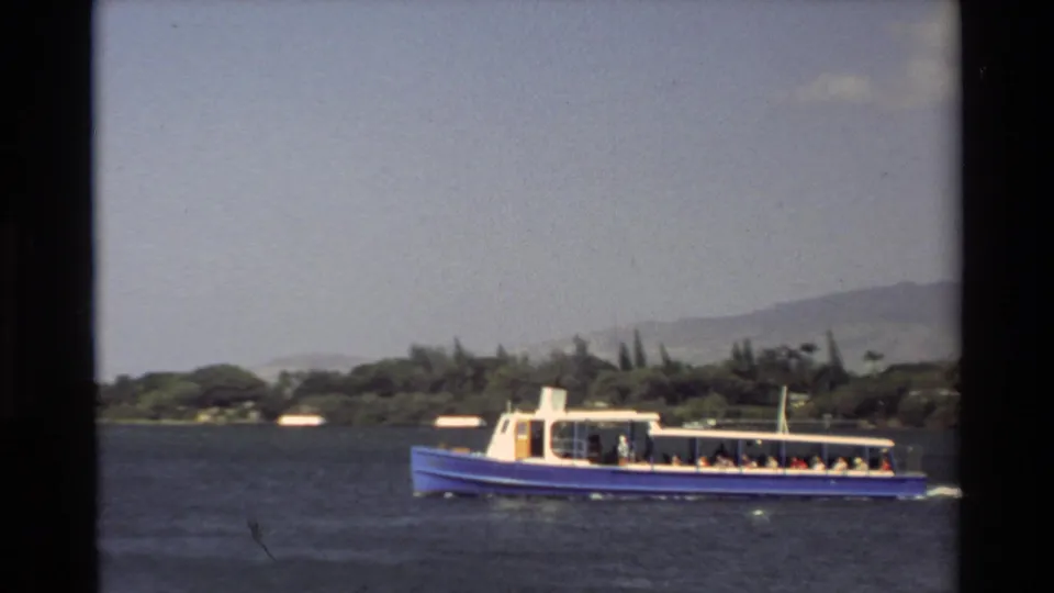 A blue-and-white tour boat carrying visible passengers moves across Pearl Harbor water in 1981 Hawaii home-movie footage.