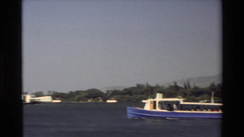 1981 Hawaii 8mm frame showing a blue passenger boat moving across tropical water near a tree-lined shore.