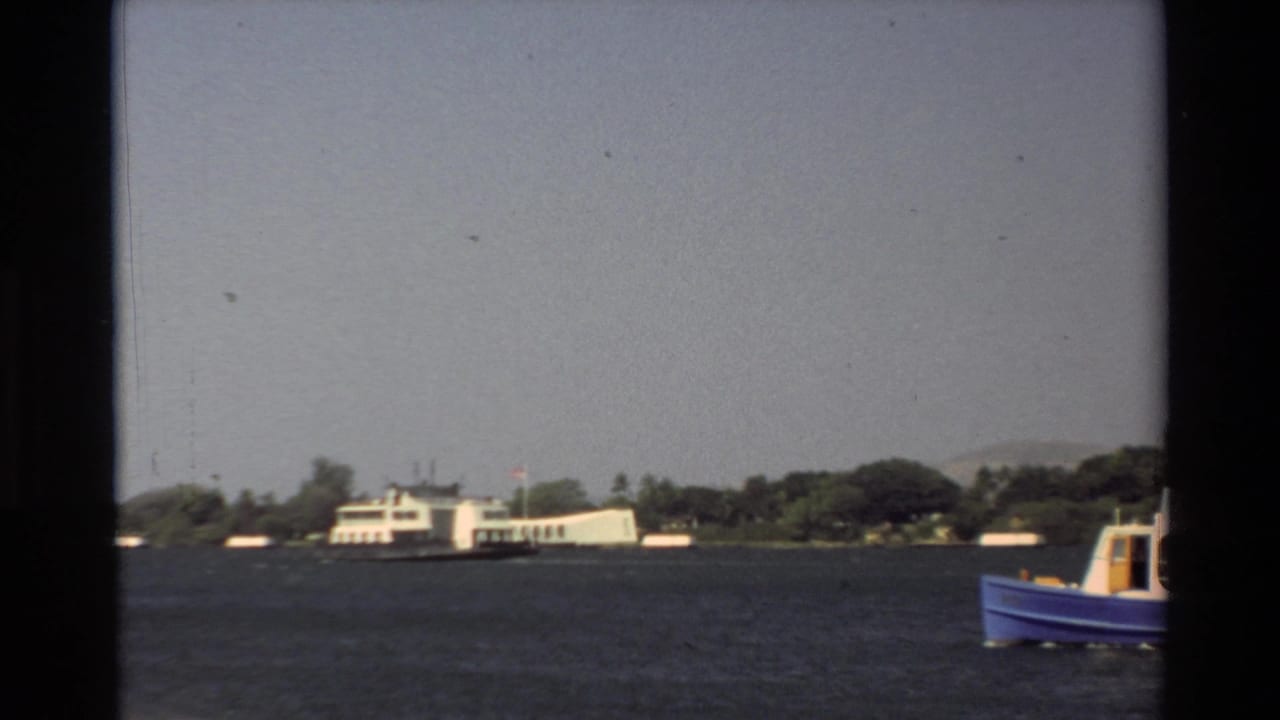 1981 Hawaii home-movie frame with a distant white ferry by the shore and a blue boat partly visible at right.
