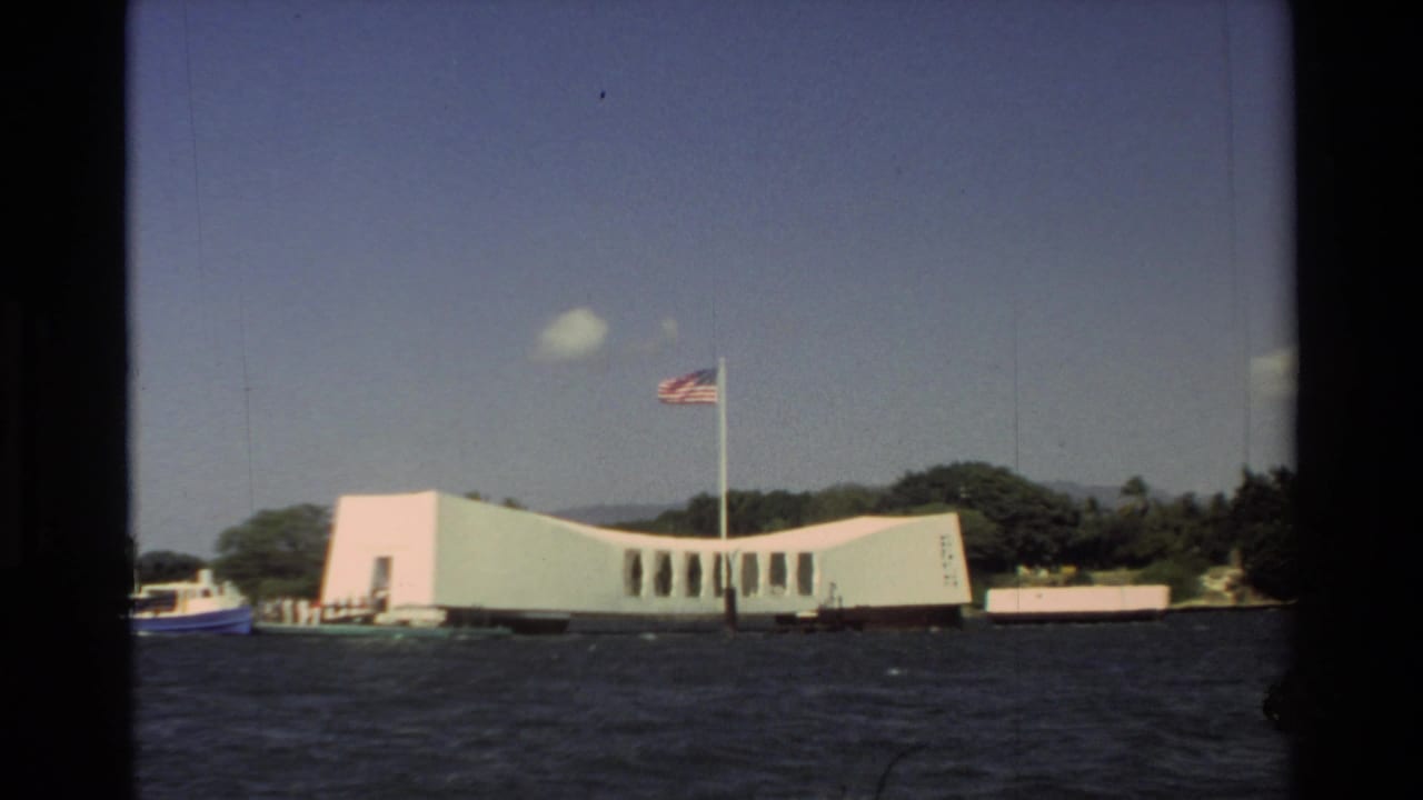 1981 Hawaii frame of the white USS Arizona Memorial seen from the water, with an American flag overhead.