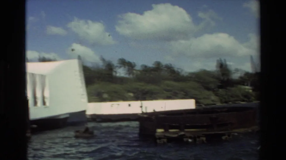 The final frame catches the edge of the USS Arizona Memorial as the boat passes, with dock structures, choppy water, clouds, and shoreline greenery.