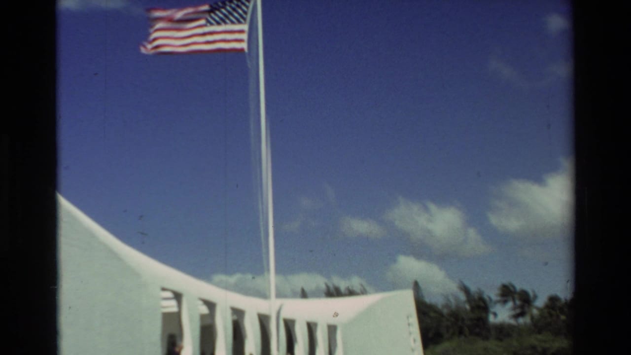 1981 Hawaii 8mm frame showing a U.S. flag flying above the white USS Arizona Memorial structure against a blue sky.