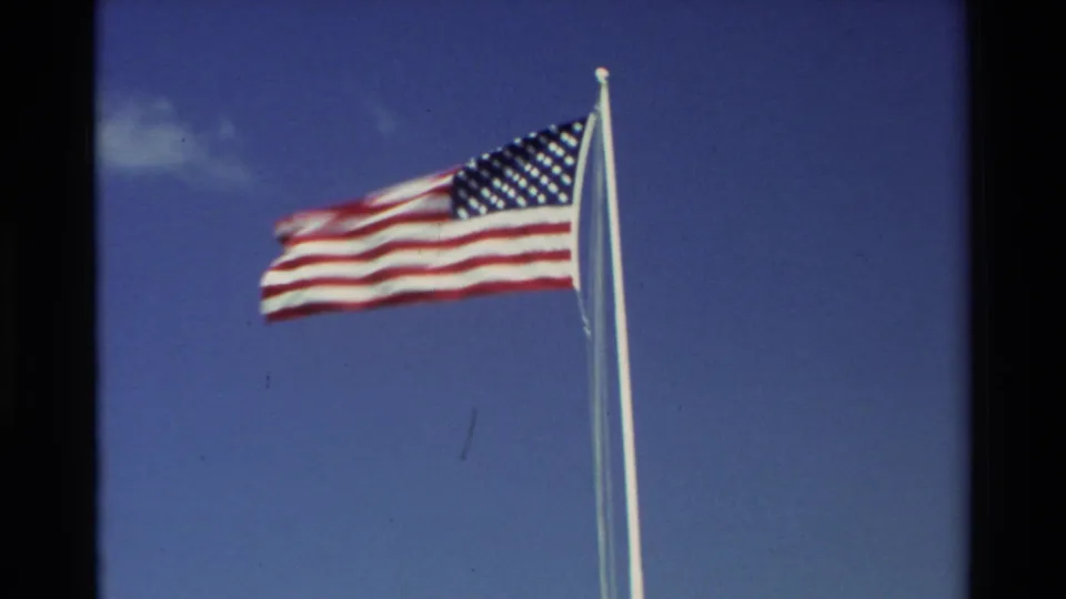 1981 Hawaii 8mm frame with a close view of the American flag waving against clear blue sky near the Pearl Harbor memorial site.