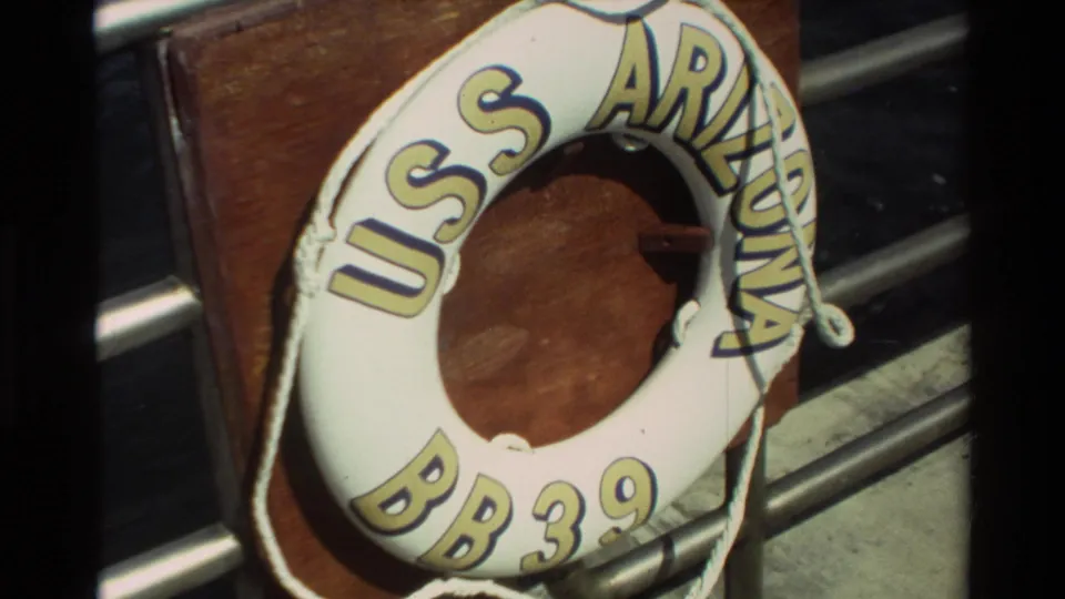 1981 Hawaii 8mm frame showing a USS ARIZONA BB39 life preserver on a wooden mount beside metal railings at the memorial site.