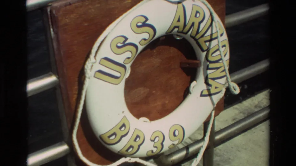 Close 1981 Hawaii 8mm view of a white USS Arizona BB 39 life ring on a wooden mount with rope and railings nearby.