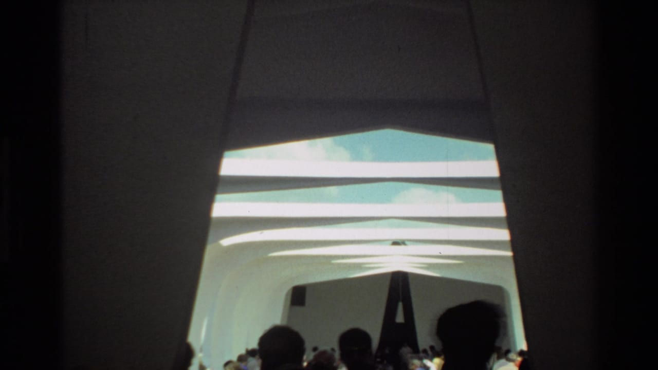 1981 Hawaii home-movie frame showing visitors walking through a white arched corridor at the USS Arizona Memorial.