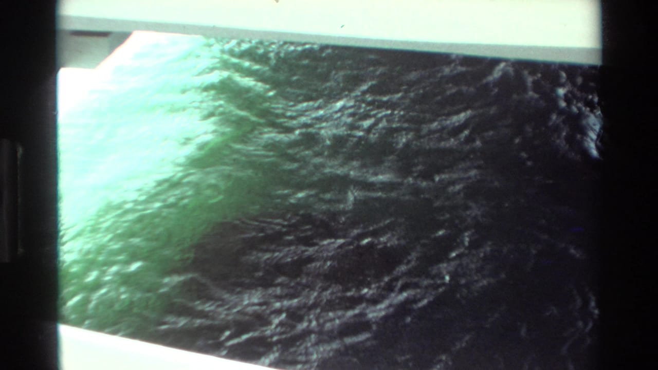 1981 Hawaii 8mm frame showing turbulent green water near a pale dock or boat edge, with heavy film borders and soft exposure.
