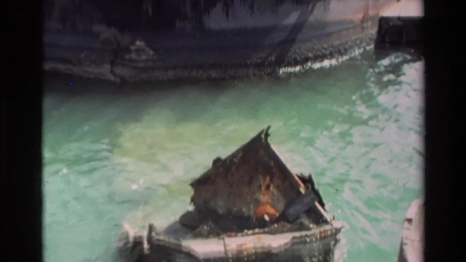 1981 Hawaii home-movie frame with a battered small boat low in pale green water beside a larger dark hull.