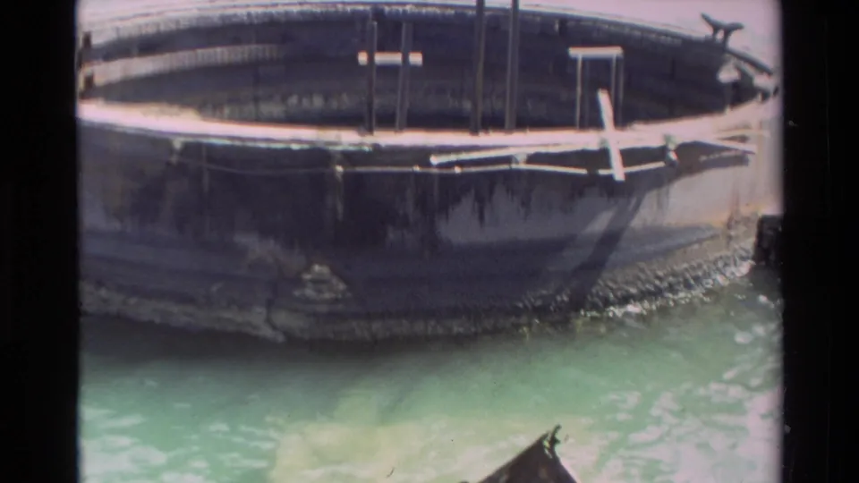 Close 8mm view of a larger dark hull over green water in Hawaii, with part of the small boat visible near the lower edge.