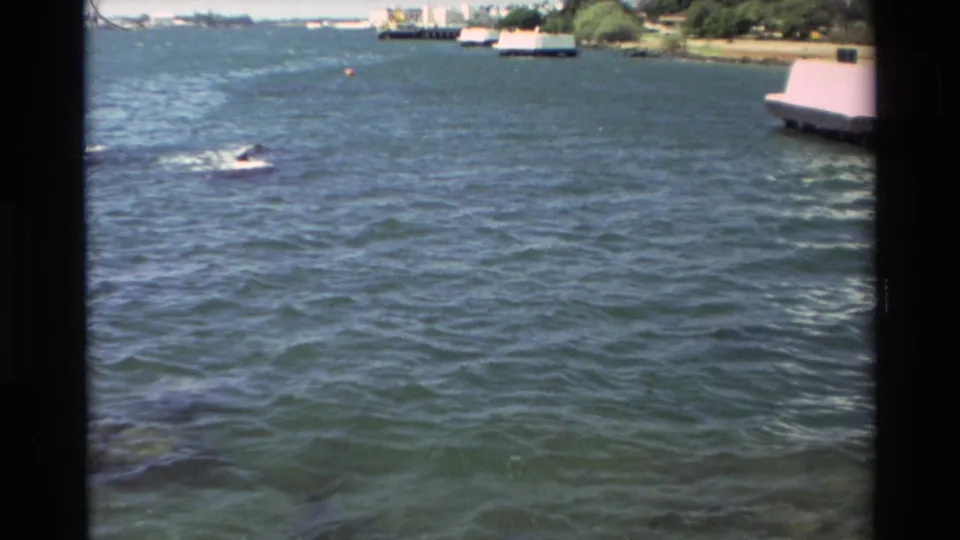 1981 Hawaii 8mm wide view over choppy water toward docks, moored boats, shoreline trees, and a small craft crossing the bay.