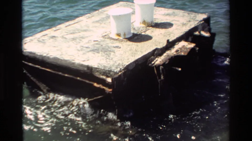 1981 Hawaii 8mm frame showing a square weathered concrete platform with two white posts as waves strike its rust-stained sides.