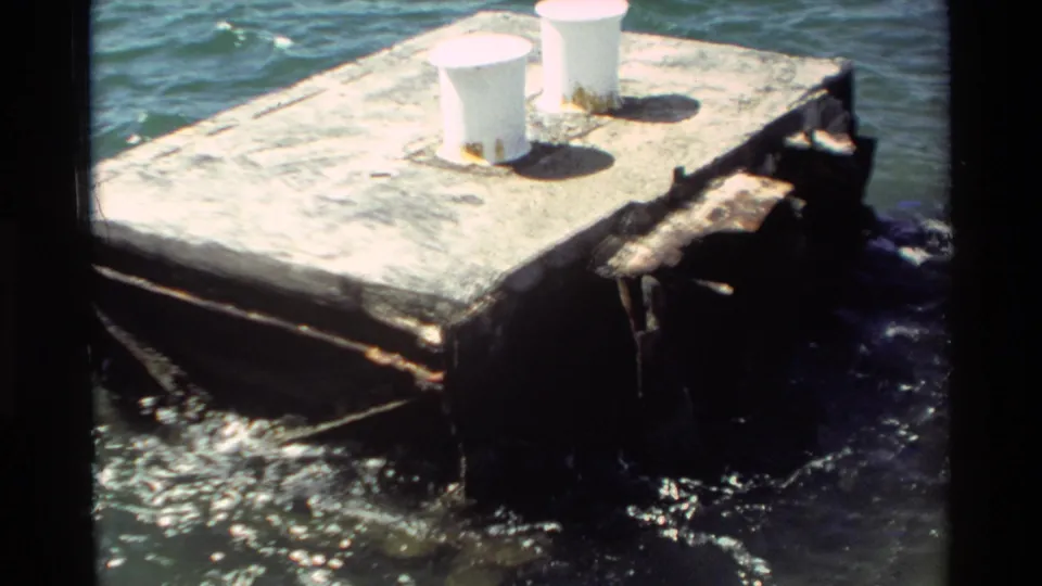 1981 Hawaii 8mm frame showing a weathered concrete pier or platform with two white bollards above harbor water.