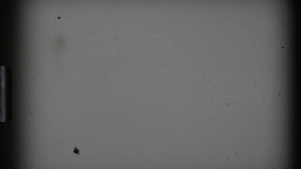 Scanned 8mm frame showing film gate edges, a gray exposed area, and visible dust before the airport scene appears.