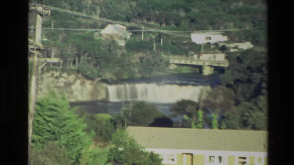 1981 New Zealand 8mm frame tightly focused on the waterfall and bridge, with power lines crossing the rural scene.