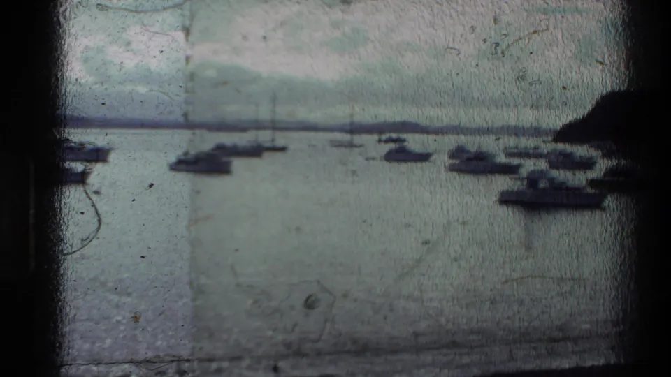 1981 New Zealand 8mm frame showing small boats at anchor in a calm bay, with a wooded hillside under cloud cover.