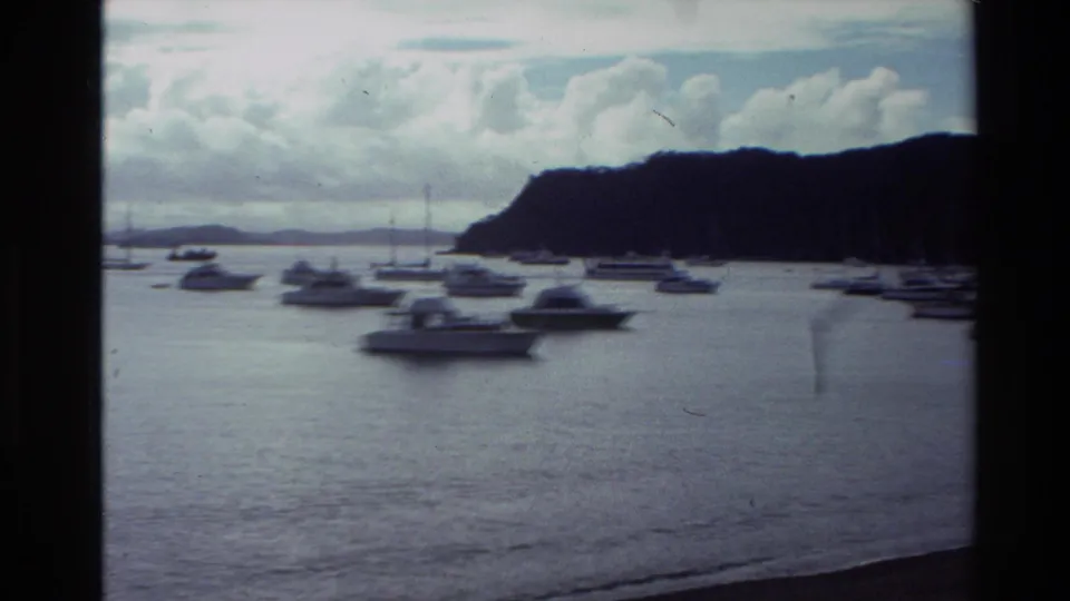 1981 New Zealand 8mm frame showing leisure boats anchored close to shore, backed by a dark wooded hillside and clouds.
