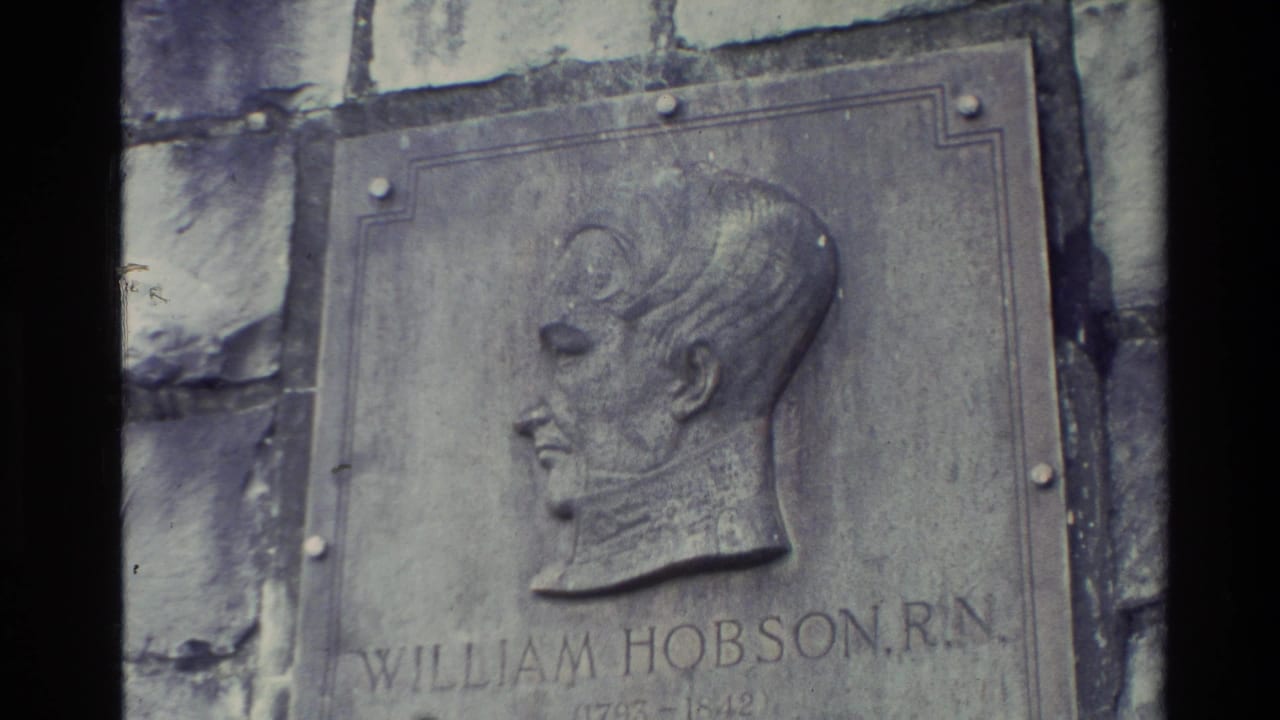 1981 New Zealand home-movie frame showing a commemorative William Hobson, R.N. plaque mounted on a stone wall.