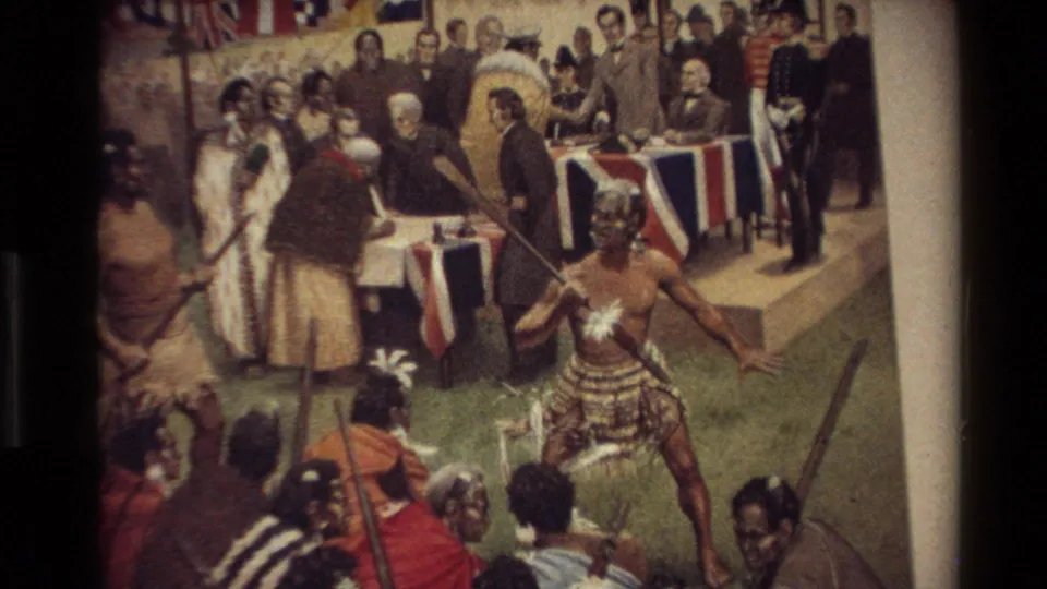 1981 New Zealand home-movie frame showing a closer view of a historical painting with Māori and European figures gathered near draped tables.