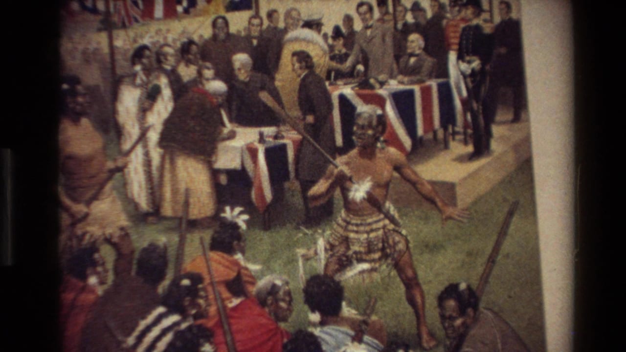 Māori performer with spear before colonial-costumed onlookers and flags.
