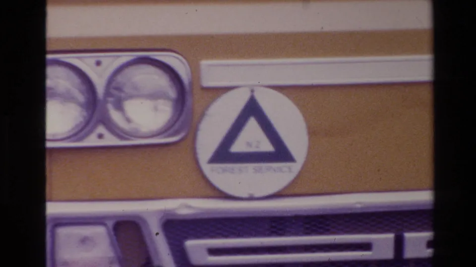 Close 1981 New Zealand frame of the yellow van front, with twin headlights, grille, bumper, and Forest Service triangle marking visible.