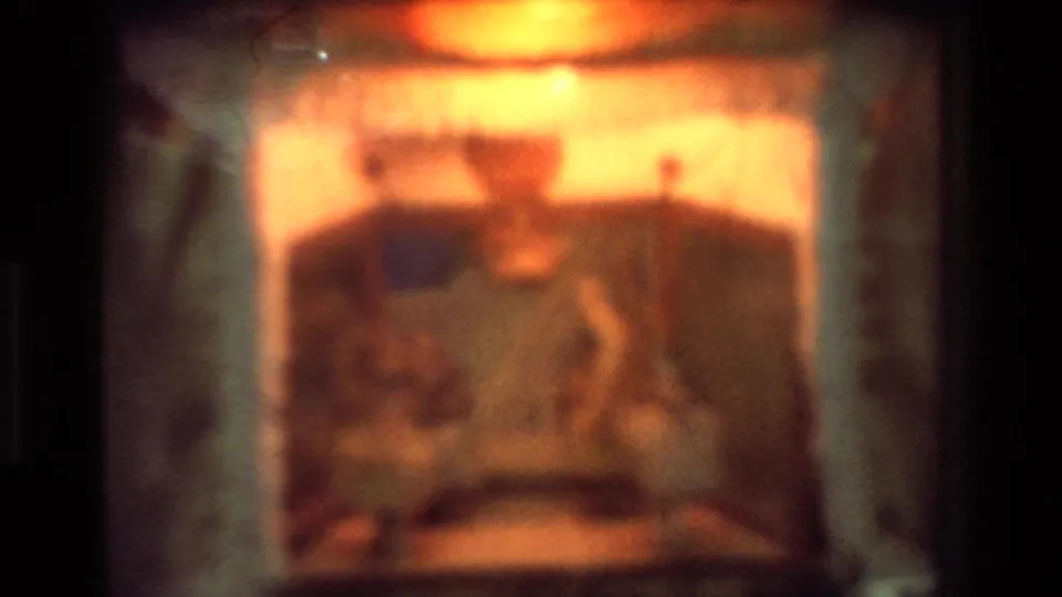 Soft, grainy close-up of the illuminated automaton-like scene inside a decorative clock or mantel object.