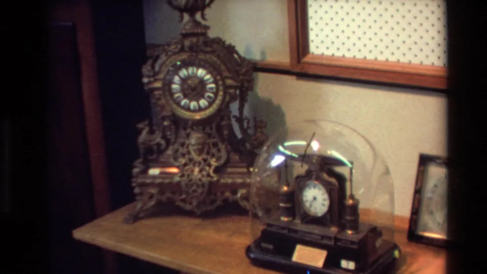 1981 New Zealand 8mm frame showing an ornate mantel clock, a smaller glass-domed clock, and framed wall decor in a private interior.