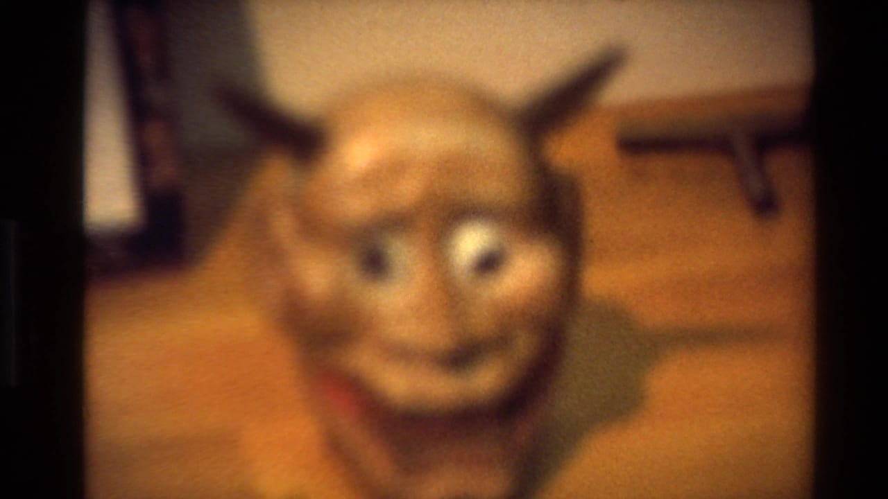 Blurred devil-like mask or figure in a warm interior shot.
