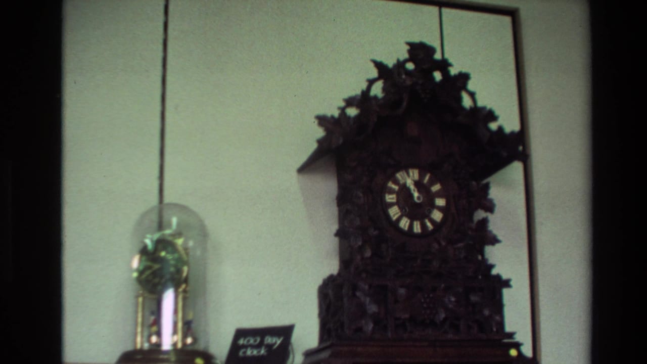 Ornate dark wooden clock beside a glass-domed clock on an indoor display shelf.