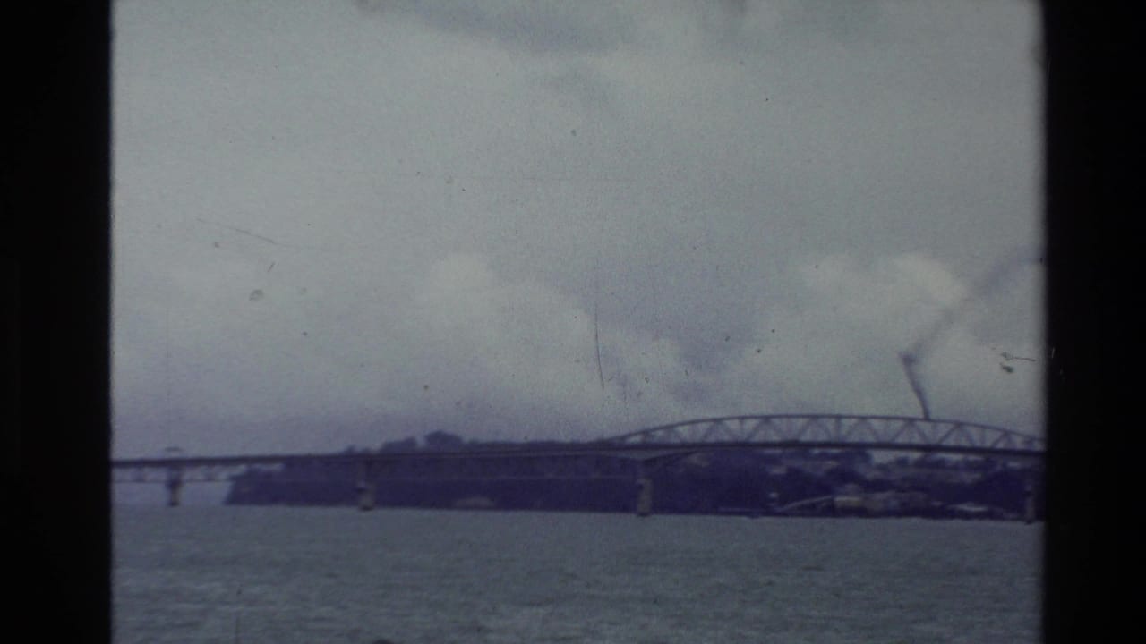 Long steel truss bridge spans rippled water beneath an overcast sky.