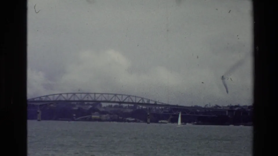 Soft 8mm frame from New Zealand in 1981 showing the bridge, water, shoreline, and cloudy sky.