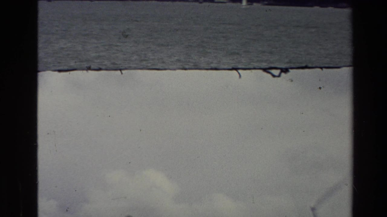 1981 New Zealand 8mm frame with a calm body of water, overcast sky, dust specks, and visible film-strip borders.