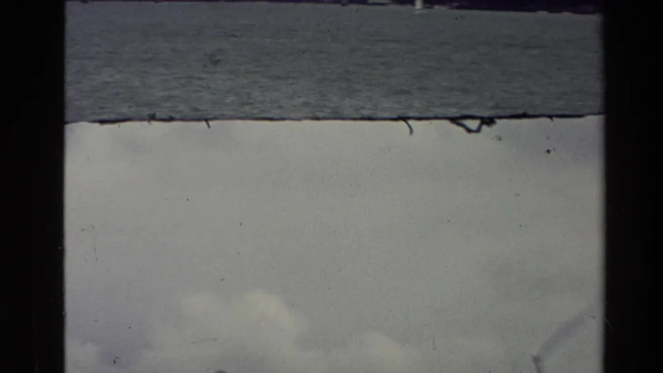1981 New Zealand 8mm frame with a calm body of water, overcast sky, dust specks, and visible film-strip borders.