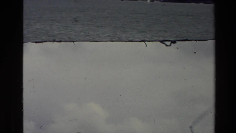 1981 New Zealand 8mm still showing grey water and cloudy sky with soft focus, dust, and dark film-frame separation.